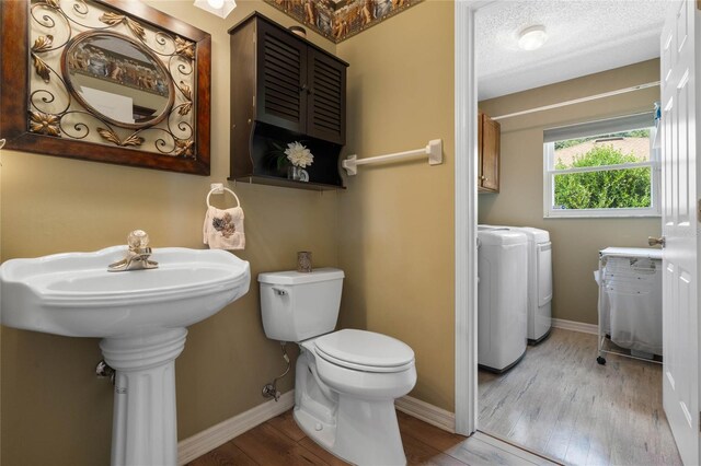 bathroom with toilet, wood-type flooring, washing machine and clothes dryer, and a textured ceiling