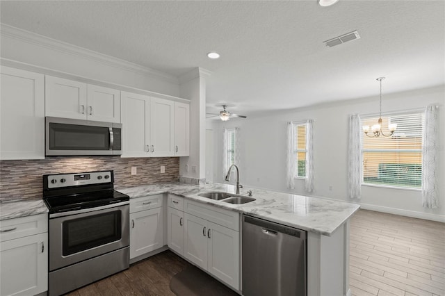 kitchen featuring kitchen peninsula, sink, white cabinetry, appliances with stainless steel finishes, and ceiling fan with notable chandelier