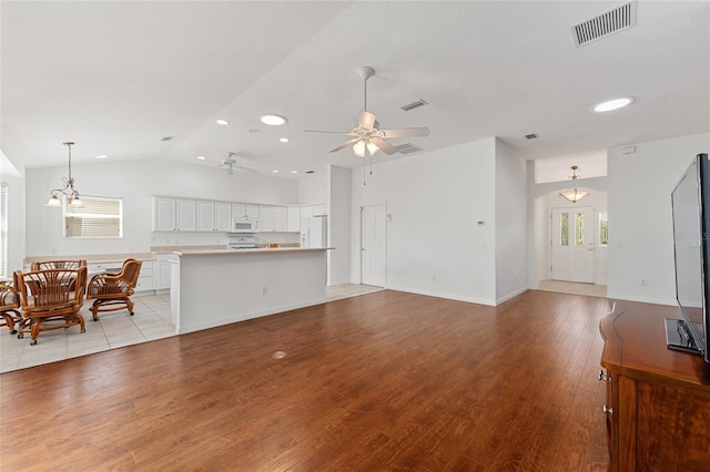 living room with lofted ceiling, a textured ceiling, ceiling fan with notable chandelier, and light hardwood / wood-style floors