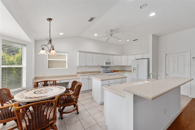 kitchen with white appliances, hanging light fixtures, white cabinetry, vaulted ceiling, and a center island with sink