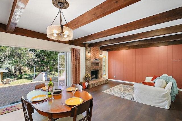 dining space with a fireplace, wooden walls, wood finished floors, a chandelier, and beamed ceiling