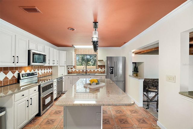 kitchen with decorative backsplash, appliances with stainless steel finishes, a center island, white cabinetry, and a sink