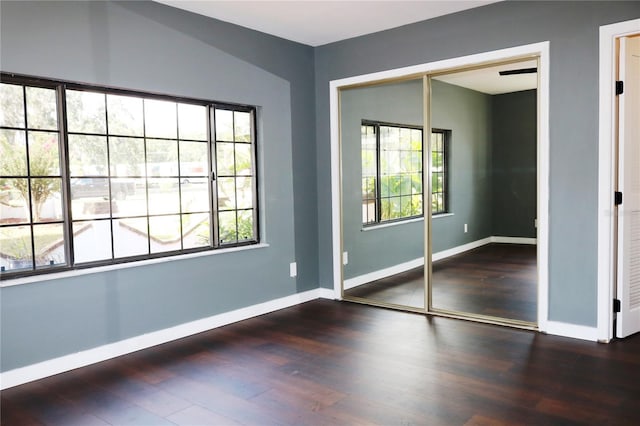 unfurnished bedroom featuring multiple windows, dark hardwood / wood-style floors, and a closet