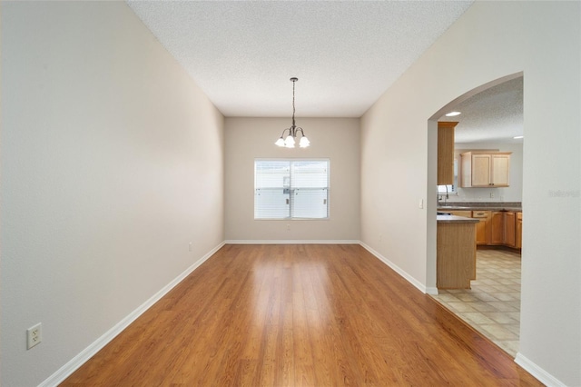 306 Bishopville Loop Unit 117, The Villages, FL 32162 - unfurnished dining area featuring a textured ceiling, arched walkways, a notable chandelier, baseboards, and light wood-style floors