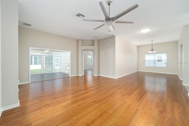 unfurnished living room with a healthy amount of sunlight, a textured ceiling, light wood-type flooring, and ceiling fan with notable chandelier