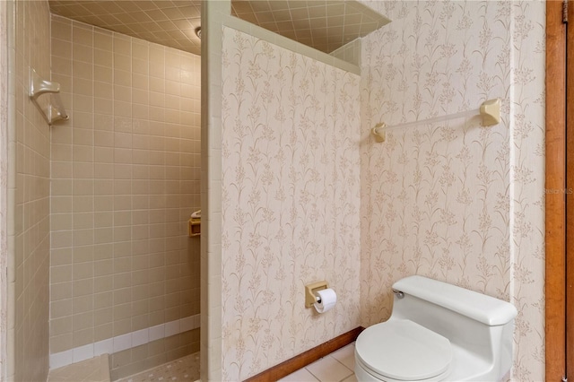 bathroom with toilet, tiled shower, and tile patterned flooring