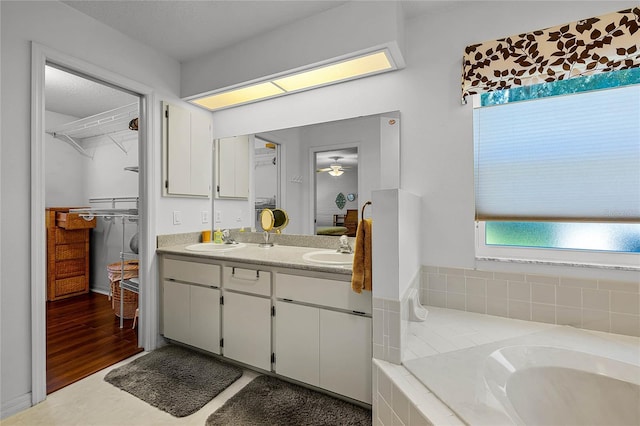 full bathroom with double vanity, a relaxing tiled tub, a walk in closet, and a sink