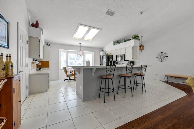 kitchen featuring stainless steel fridge, white cabinetry, a kitchen bar, kitchen peninsula, and lofted ceiling