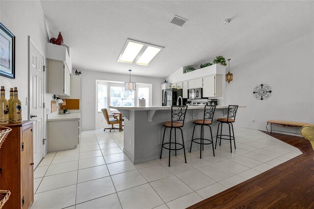 kitchen with light tile patterned floors, visible vents, a breakfast bar, fridge, and black microwave