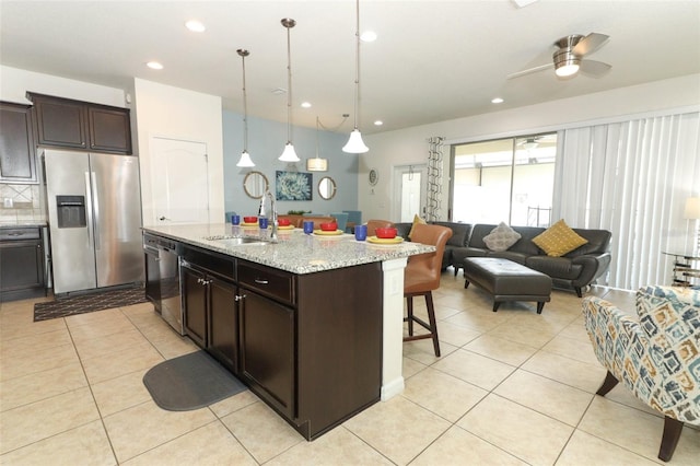 kitchen with an island with sink, sink, light stone countertops, ceiling fan, and appliances with stainless steel finishes