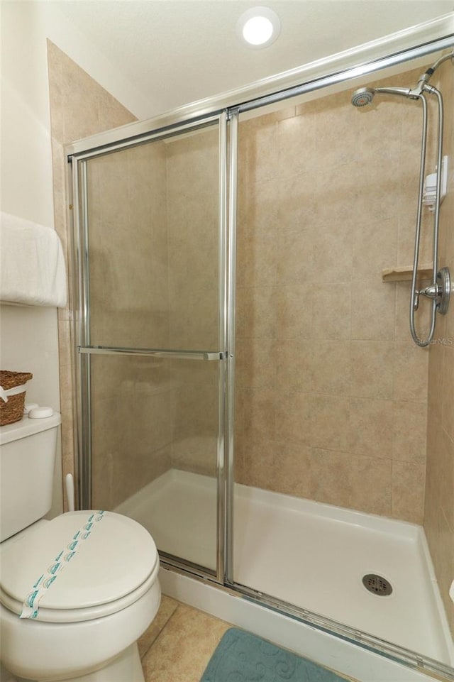 bathroom with a shower with door, toilet, and tile patterned flooring