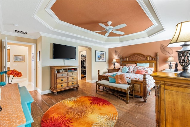 bedroom featuring ceiling fan, a walk in closet, ornamental molding, and a tray ceiling