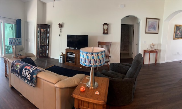 living area with arched walkways, wood finished floors, and baseboards