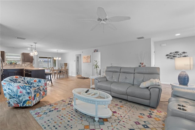 living room featuring ceiling fan with notable chandelier and light hardwood / wood-style floors