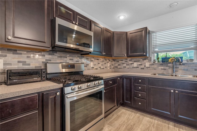 kitchen featuring light wood-type flooring, backsplash, stainless steel appliances, and sink