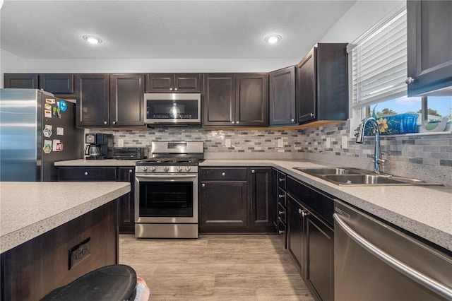 kitchen with tasteful backsplash, sink, appliances with stainless steel finishes, and light hardwood / wood-style floors