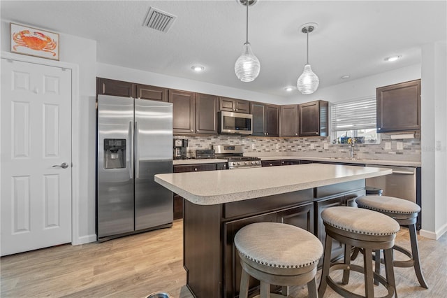 kitchen featuring a kitchen island, backsplash, light hardwood / wood-style floors, hanging light fixtures, and stainless steel appliances