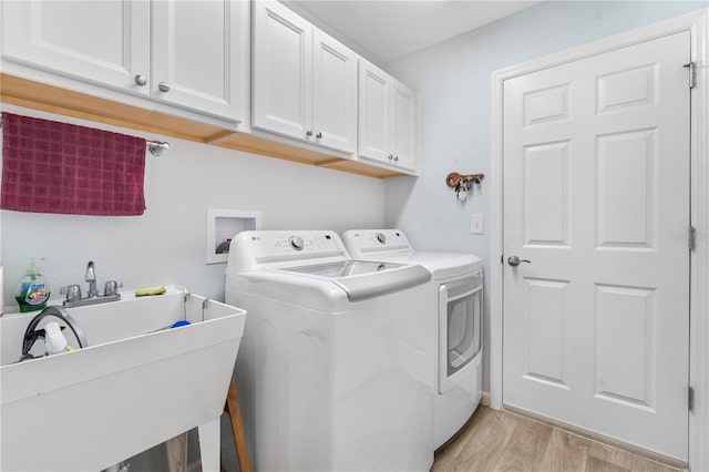 clothes washing area with light wood-type flooring, washing machine and clothes dryer, cabinets, and sink