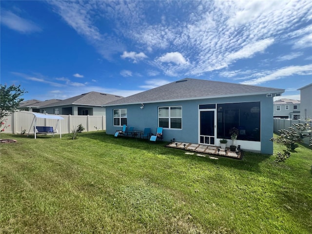 back of property with fence, a sunroom, a shingled roof, stucco siding, and a lawn