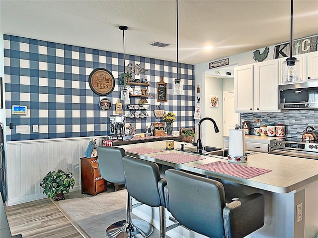 kitchen featuring appliances with stainless steel finishes, white cabinetry, hanging light fixtures, and a kitchen breakfast bar