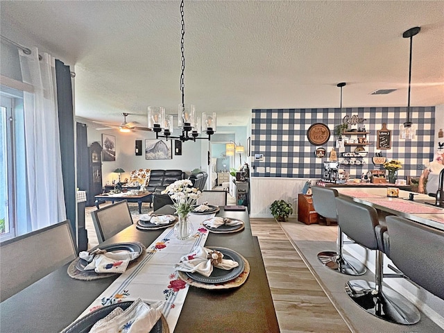 dining room with ceiling fan with notable chandelier, a textured ceiling, and light hardwood / wood-style flooring