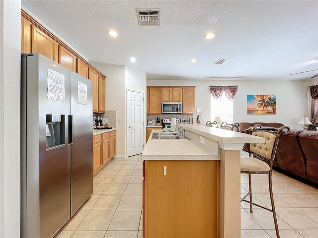 kitchen with a kitchen bar, sink, appliances with stainless steel finishes, a center island with sink, and light tile patterned flooring