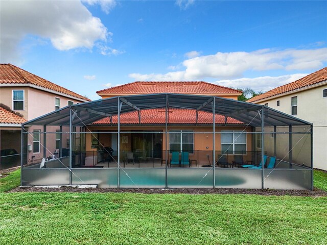 rear view of house with glass enclosure, a lawn, and a patio