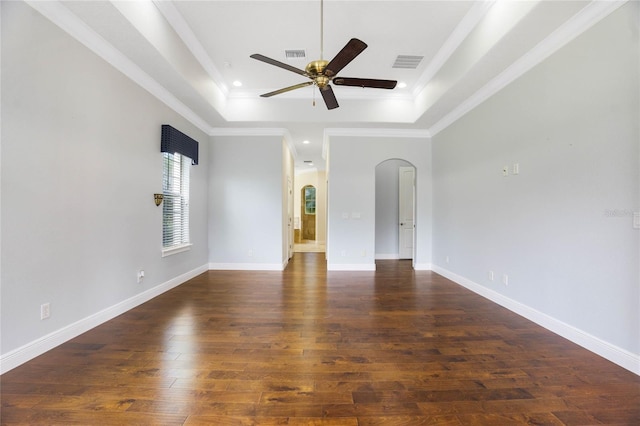 empty room featuring arched walkways, wood finished floors, visible vents, ornamental molding, and a tray ceiling