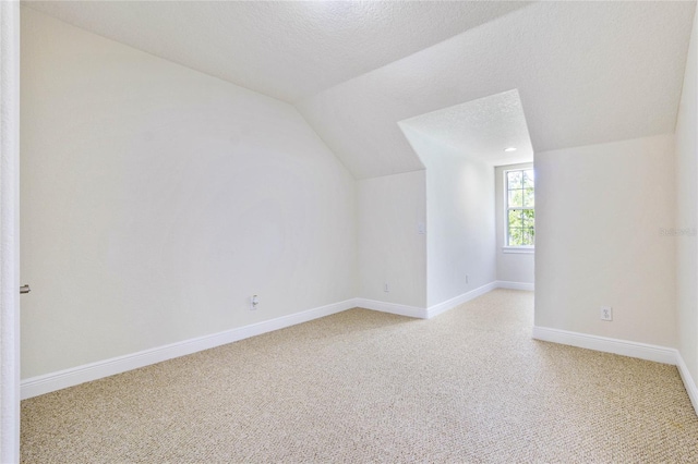 additional living space with a textured ceiling, vaulted ceiling, light colored carpet, and baseboards