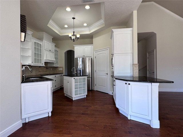 kitchen featuring open shelves, dark countertops, a raised ceiling, a sink, and wall chimney exhaust hood