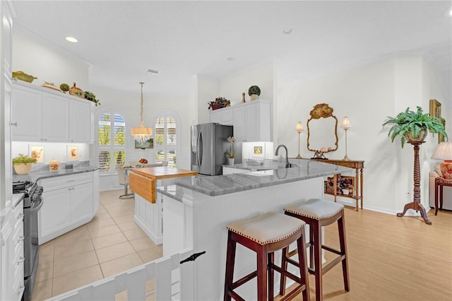 kitchen featuring a kitchen breakfast bar, light stone counters, appliances with stainless steel finishes, white cabinets, and light hardwood / wood-style floors