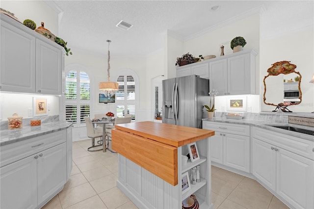 kitchen featuring stainless steel refrigerator with ice dispenser, crown molding, white cabinetry, light stone counters, and light tile patterned flooring