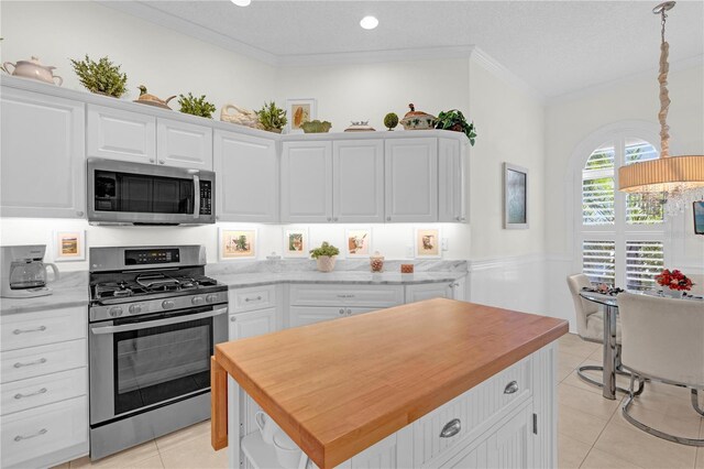 kitchen featuring white cabinetry, a kitchen island, wood counters, appliances with stainless steel finishes, and light tile patterned flooring