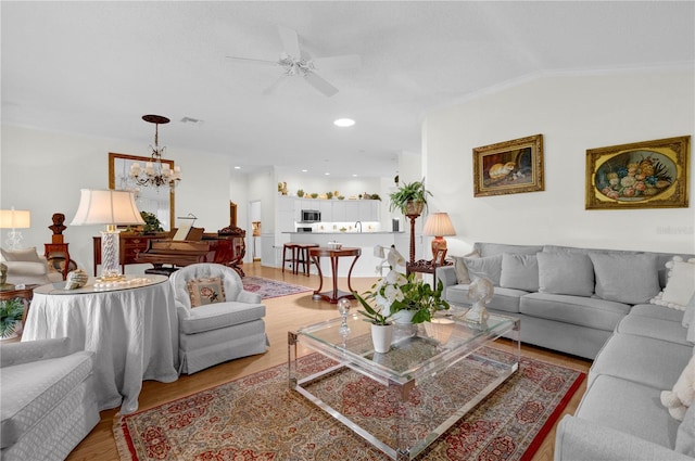 living room with light wood-type flooring, ceiling fan with notable chandelier, lofted ceiling, and ornamental molding