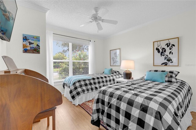 bedroom featuring a textured ceiling, light hardwood / wood-style flooring, ceiling fan, and ornamental molding