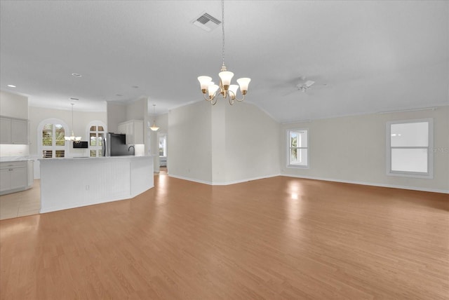 unfurnished living room featuring baseboards, visible vents, vaulted ceiling, light wood-type flooring, and ceiling fan with notable chandelier