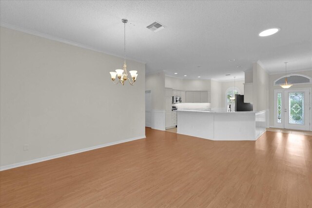 unfurnished living room featuring ornamental molding, light wood-type flooring, visible vents, and baseboards