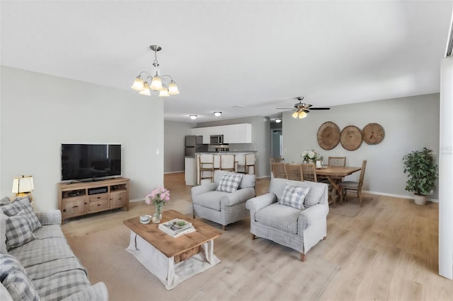 living room featuring ceiling fan with notable chandelier and light hardwood / wood-style flooring