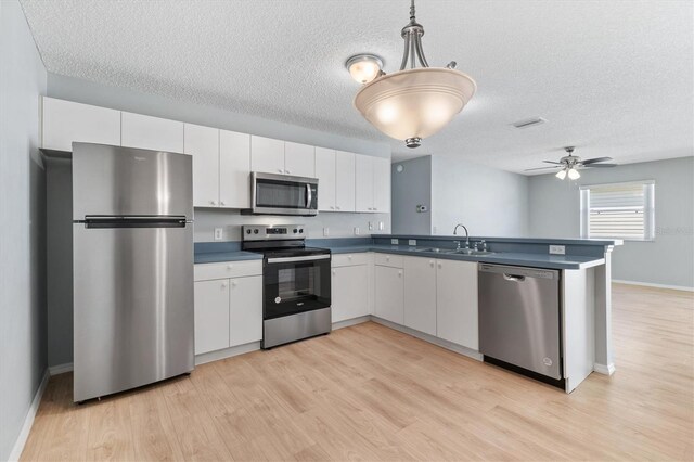 kitchen with stainless steel appliances, kitchen peninsula, sink, ceiling fan, and white cabinets