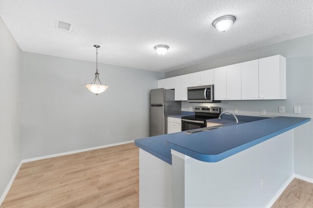 kitchen featuring decorative light fixtures, appliances with stainless steel finishes, kitchen peninsula, and light hardwood / wood-style flooring