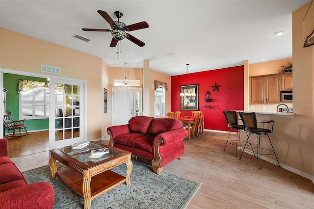 living room with light wood-type flooring, ceiling fan with notable chandelier, and a healthy amount of sunlight