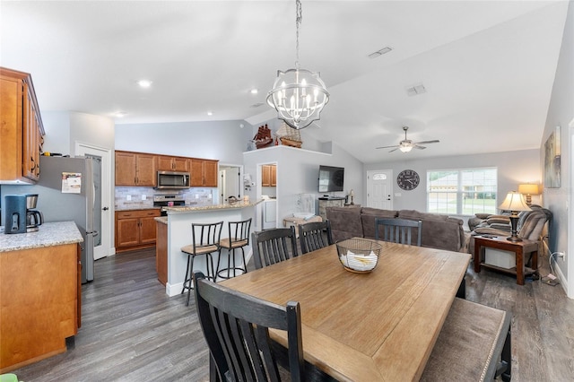 dining area with ceiling fan with notable chandelier, vaulted ceiling, and dark hardwood / wood-style flooring