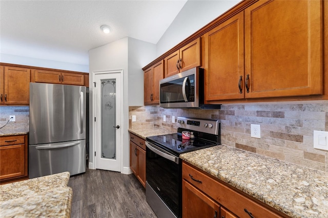 kitchen with vaulted ceiling, light stone countertops, dark hardwood / wood-style flooring, appliances with stainless steel finishes, and decorative backsplash