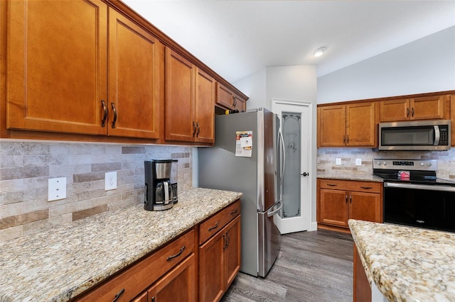 kitchen featuring wood-type flooring, light stone counters, stainless steel appliances, and decorative backsplash