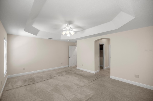 empty room featuring a tray ceiling, light colored carpet, and ceiling fan