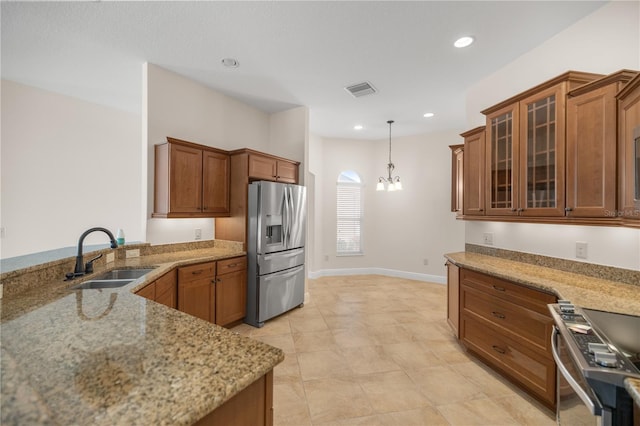 kitchen with hanging light fixtures, sink, light stone countertops, an inviting chandelier, and appliances with stainless steel finishes