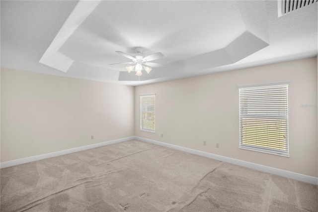 unfurnished room with a textured ceiling, light colored carpet, a tray ceiling, and ceiling fan