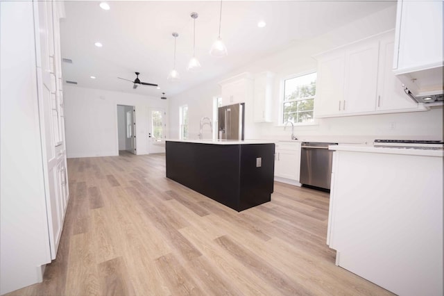 kitchen featuring pendant lighting, white cabinets, light wood-type flooring, appliances with stainless steel finishes, and a kitchen island