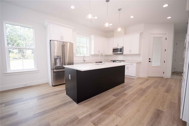 kitchen with white cabinetry, hanging light fixtures, stainless steel appliances, light hardwood / wood-style floors, and a kitchen island with sink