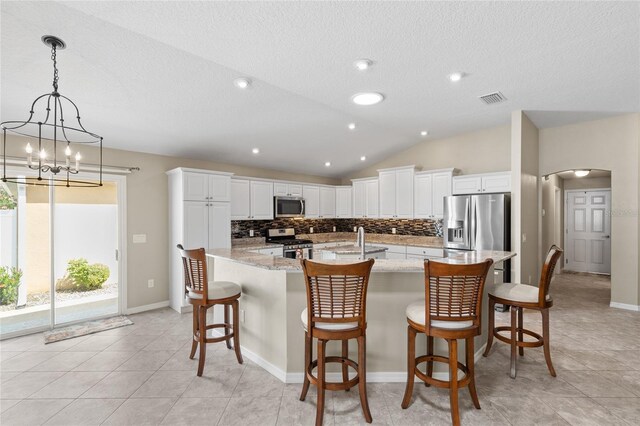 kitchen featuring light stone countertops, white cabinets, stainless steel appliances, decorative backsplash, and vaulted ceiling